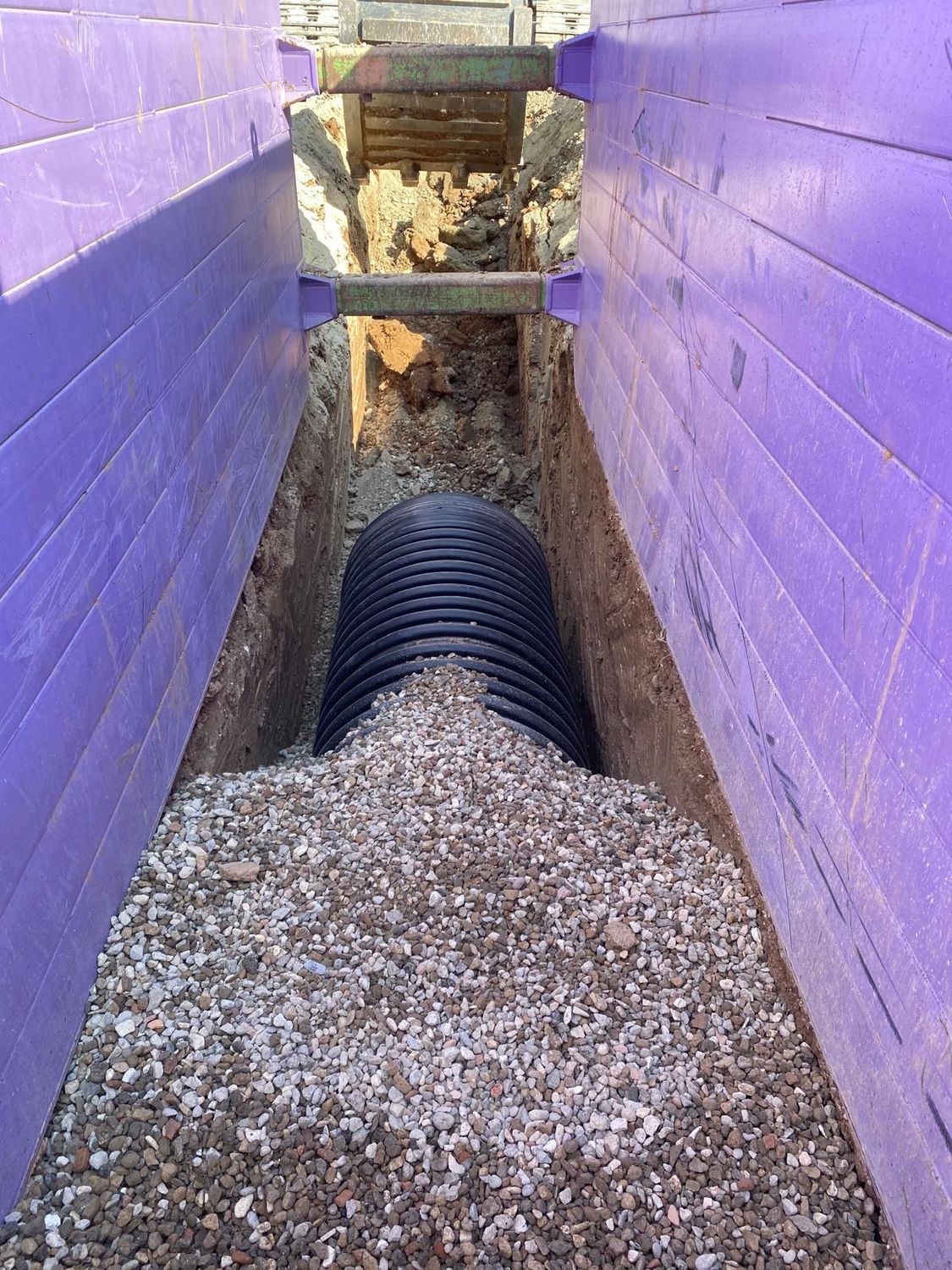Twin wall pipe bedded in gravel inside a trench box