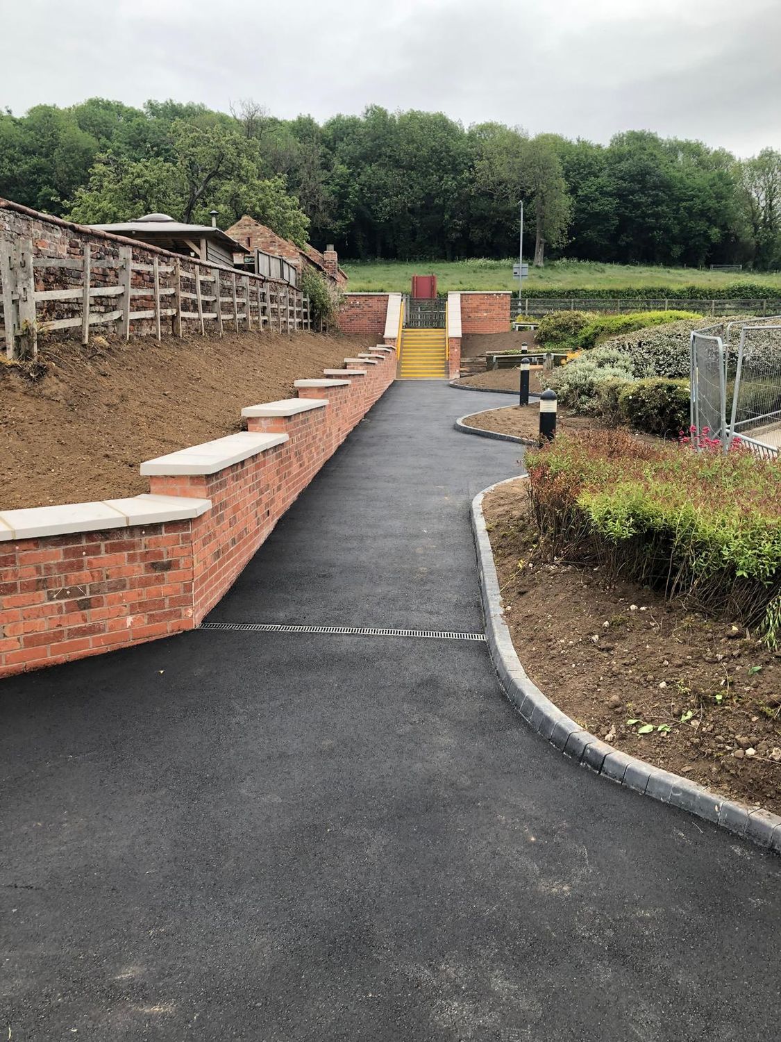 The new tarmac path with a brick retaining wall and kerb edging